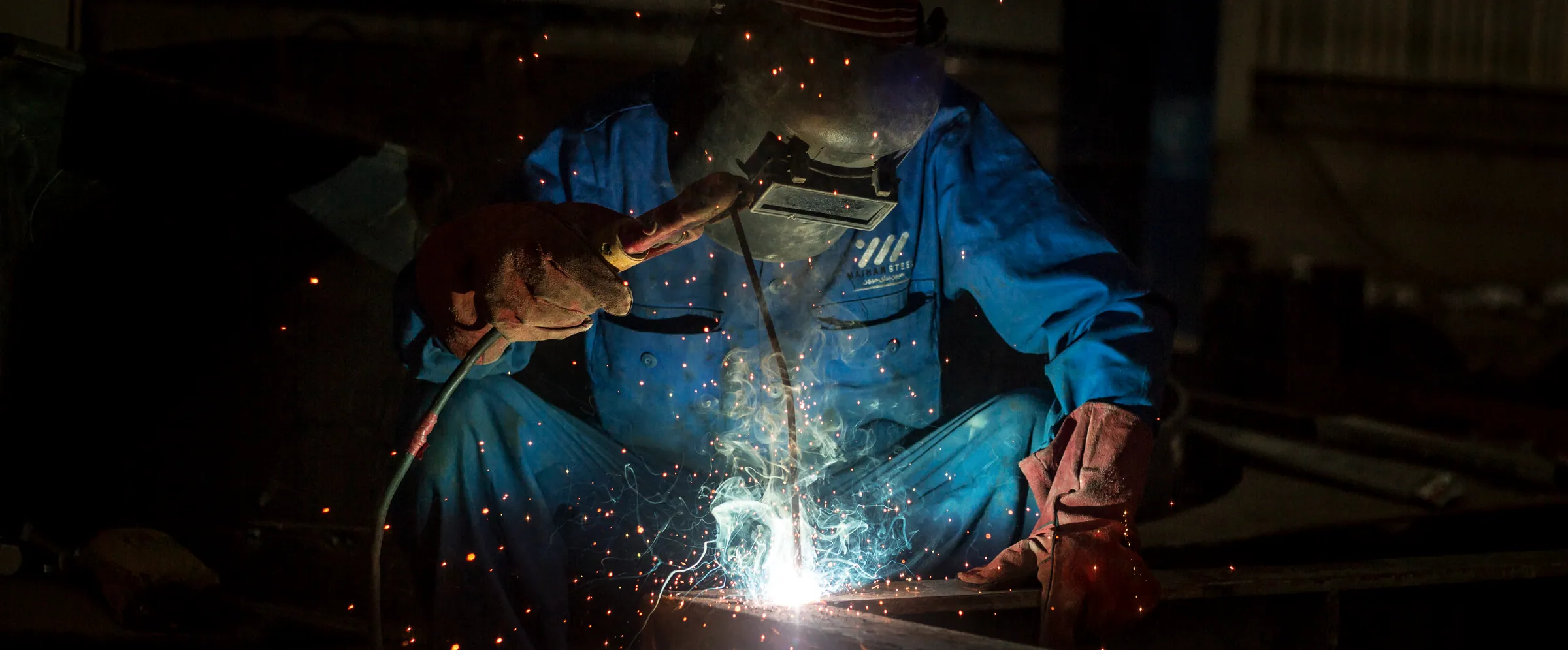 Welder in a Maihan Steel uniform at work, sparks around the weld